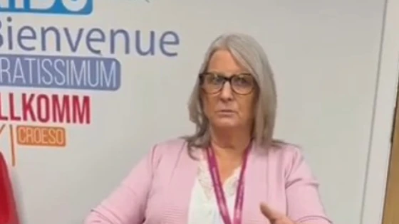 Woman with grey hair and glasses speaking in a pink chair, with a welcome wall behind and subtitles about SQA. Woman with grey hair and glasses speaking in a pink chair, with a welcome wall behind and subtitles about SQA.